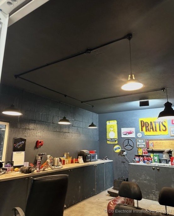 Pendant lights suspended from an exposed black conduit grid in a barber shop