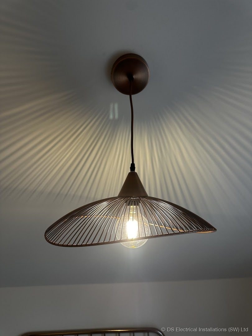 Copper wire framed conical pendant light hung and lit, viewed from the side