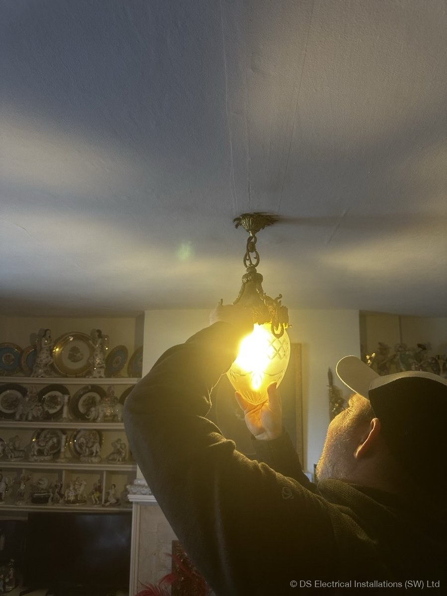 Electrician offering up an ornate period ceiling pendant to a newly wired ceiling rose