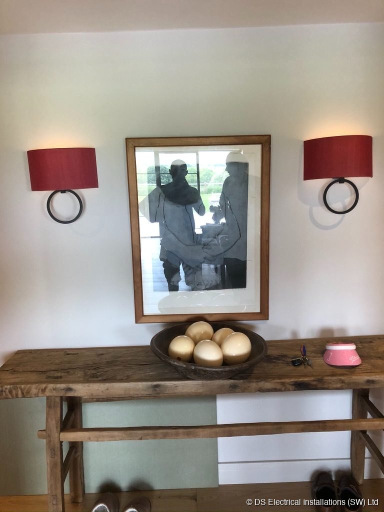 Red silk drum wall sconces wired either side of framed artwork in a period hallway