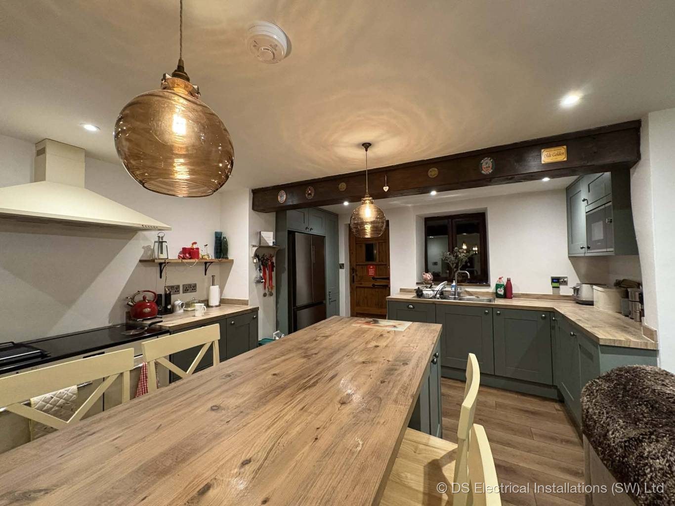 Amber glass globe pendants and downlights over a kitchen-diner table with an exposed beam
